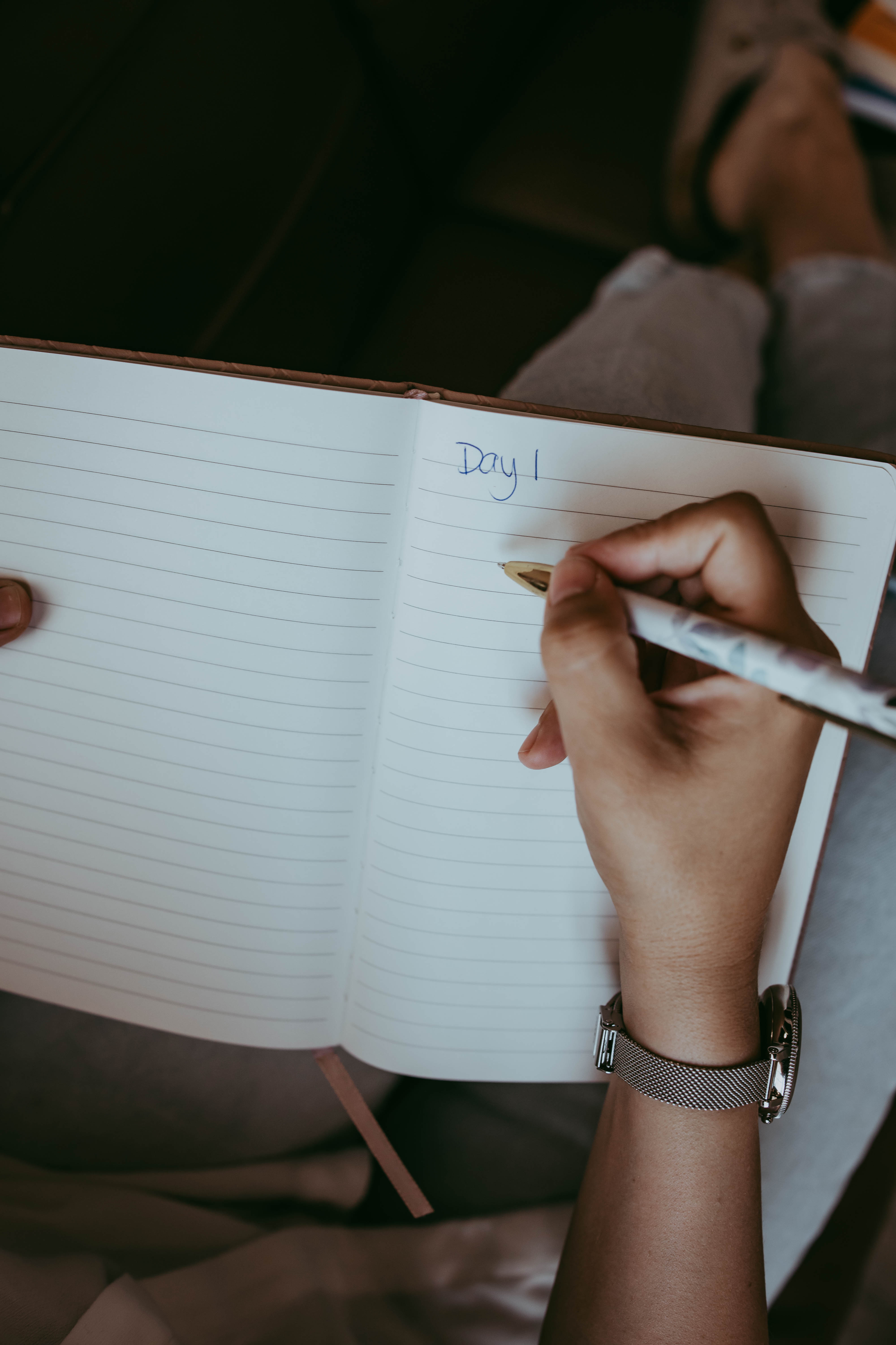 A person wearing a silver watch writes "Day 1" in a lined journal during a Theraplay session reflection.